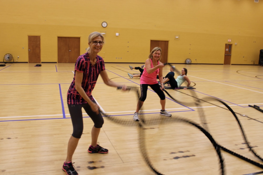 Two women smiling and looking at the camera while swinging large black ropes